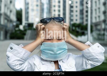 Petite fille blanche blonde portant un masque facial de protection se sentir stressée et les cris malheureux et pleurs dus à la quarantaine et à la pandémie de covid-19 nouveau Banque D'Images