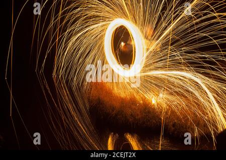 Vue arrière d'un homme debout dans un parc sombre avec des couleurs vives flammes avec effet longue exposition Banque D'Images