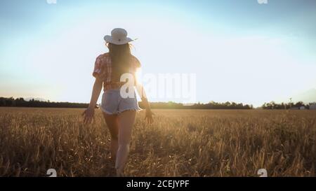 Bonne femme courir sur un champ de blé avec les bras ouverts au soleil couchant. Banque D'Images