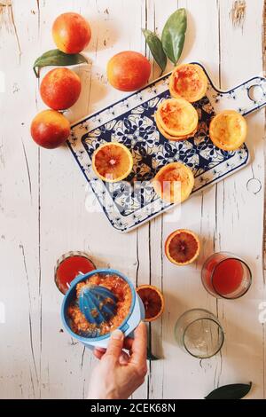 Main de femme préparant du jus d'orange de sang sur une table en bois blanc Banque D'Images