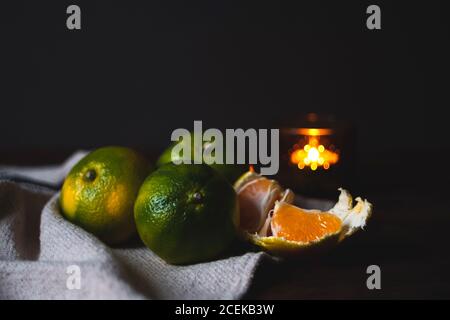 Mandarines vertes fraîches près des agrumes mûrs pelés placés sur le plat chiffon sur fond noir et lumière floue Banque D'Images