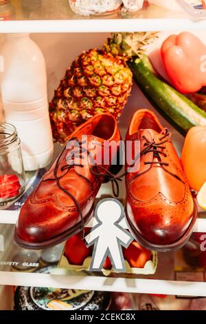 Au-dessus de la silhouette de papier pour l'April Fools Day près de chaussures, les oeufs dans un récipient et de l'alimentation sur des étagères au réfrigérateur Banque D'Images