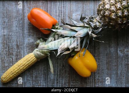 PARTY MIX: Un mélange de fruits et de légumes qui comprennent des poivrons, de l'ananas, et du maïs sur l'épi sont disposés ensemble sur une planche à découper en bois. Banque D'Images