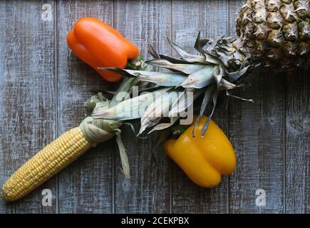 PARTY MIX: Un mélange de fruits et de légumes qui comprennent des poivrons, de l'ananas, et du maïs sur l'épi sont disposés ensemble sur une planche à découper en bois. Banque D'Images