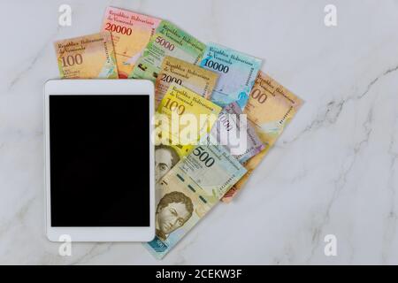 Série Tablet PC de billets avec différentes devises de billets papier Bolivar vénézuélien sur la table Banque D'Images