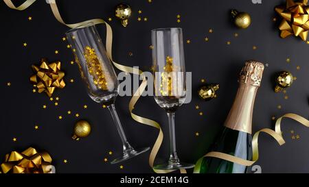 Composition de Noël. Fond de Noël noir avec bouteille de champagne, verres, boules dorées et décorations, confetti. Flat lay, vue de dessus. Banque D'Images