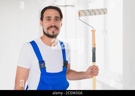 Un homme barbu dans une combinaison bleue tient un rouleau dans sa main et pose à la caméra Banque D'Images