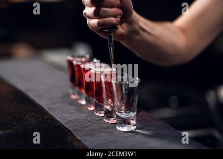 le barman verse de l'alcool rouge dans des coups de feu sur le bar, le spectacle du barman. Banque D'Images