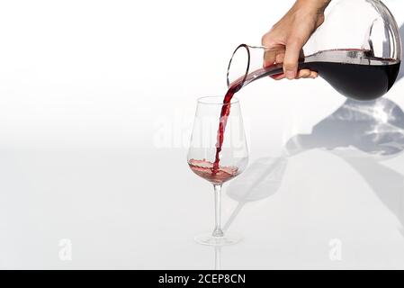 Le sommelier verse du vin rouge de la carafe au vin sur fond blanc. Banque D'Images