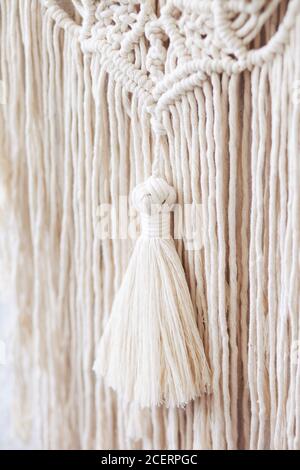 Décoration murale 100% coton macrame fait à la main sur un mur blanc. Fils de coton et de tressage en macrame. Gros plan sur les détails. Passe-temps féminin. Banque D'Images