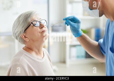 Travailleur médical professionnel portant un équipement de protection personnelle testant une femme âgée pour les maladies respiratoires à l'aide d'une baguette de test Banque D'Images