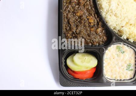 Délicieuse cuisine nord-indienne Chana Masala, riz, Boondi Raita dans une plaque en plastique sur fond blanc Banque D'Images