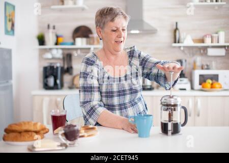 Femme mature utilisant la presse française pour faire du café dans la cuisine pendant le petit déjeuner. Personne âgée dans la matinée en appréciant café frais brun expresso tasse de caféine de la tasse vintage, filtre relax rafraîchissement Banque D'Images