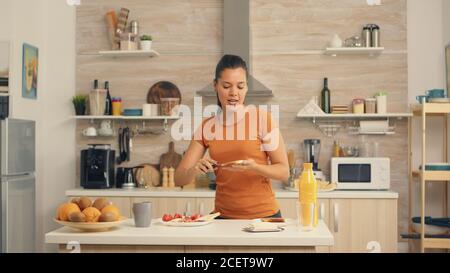 Une femme joyeuse dansant le matin et répandant du beurre sur du pain rôti. Couteau d'étalement de beurre doux sur une tranche de pain. Un style de vie sain, pour un délicieux repas du matin dans une cuisine confortable. Déjeuner traditionnel savoureux Banque D'Images