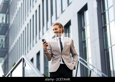 Portrait d'un jeune homme d'affaires prospère. Un homme aux cheveux bouclés dans une chemise blanche avec un téléphone sur le fond d'un centre d'affaires moderne Banque D'Images