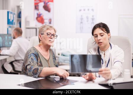 Médecin discutant avec le patient senior tenant des rayons X dans le bureau de l'hôpital. Femme mature écoutant médecin diagnostic. Banque D'Images