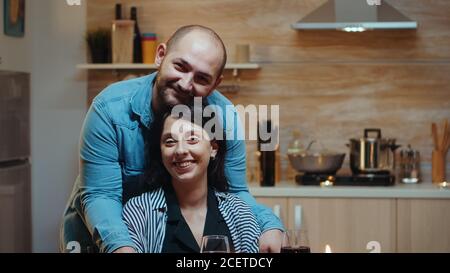 Portret de couple gai regardant la caméra, souriant, assis à table dans la cuisine pendant le dîner romantique. Heureux mariés poeple moments spéciaux de soumission, de plaisir le repas à la fête des bougies Banque D'Images