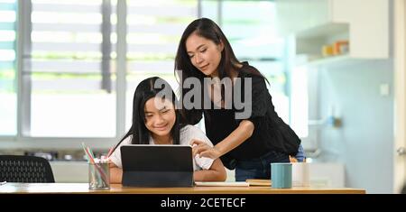 Une jeune mère enseigne à une fille de faire ses devoirs à la table en bois. Banque D'Images