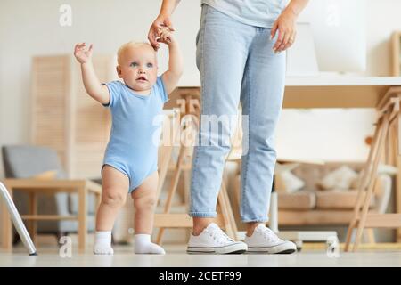 Plan horizontal de mère méconnaissable tenant peu de main d'elle un adorable enfant qui essaie de marcher à la maison Banque D'Images