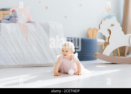 Un joli blond aux yeux bleus bébé d'un an une robe rose est tenue rampant sur tous les farines dedans la chambre des enfants à l'étage Banque D'Images