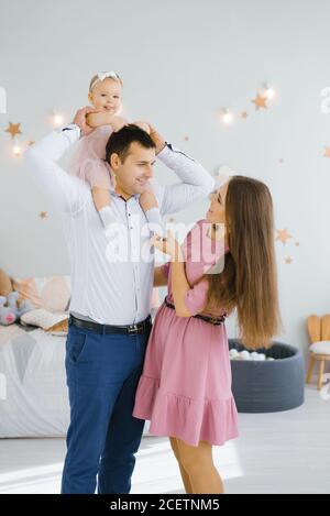 La fille sourit et roule sur le cou de son père. Une maman heureuse se tient à côté Banque D'Images