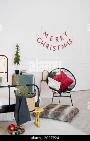 Décoration de Noël dans la chambre : chaise avec oreillers, branches de pin et de sapin, sapin de Noël sur la table de nuit et inscription « Joyeux Noël » Banque D'Images