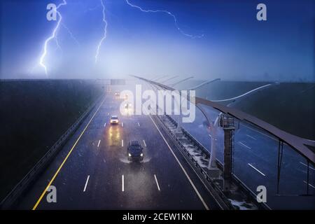 Voitures roulant sur une autoroute dans une pluie battante avec un orage. Tempête, foudre et brouillard sur route sombre Banque D'Images
