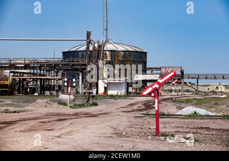 Ancien réservoir de stockage de pétrole rouillé et panneau ferroviaire cassé sur l'ancienne usine soviétique (usine) sur fond bleu ciel. Banque D'Images