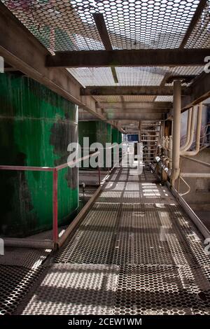 Réservoir en métal, tuyaux et raccords sur l'ombre du sol en maille. Vue abstraite sur la plante chimique. Engrais phosphate plante. Banque D'Images