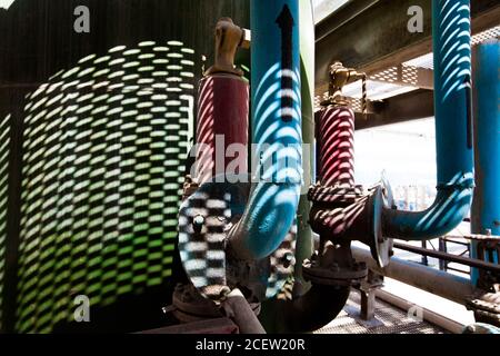 Réservoir en métal, tuyaux et raccords sur l'ombre du sol en maille. Vue rapprochée abstraite de l'usine chimique. Banque D'Images