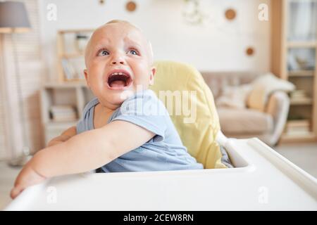 Portrait horizontal moyen en gros plan de bébé méchant assis chaise haute pleurant quelque chose Banque D'Images