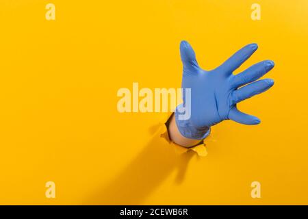 Main dans un gant de latex saisissant quelque chose par le jaune déchiré mur Banque D'Images