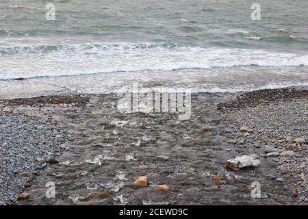 Point où un ruisseau rencontre la mer bâclée sur une plage rocheuse à Trefor, au nord du pays de Galles Banque D'Images