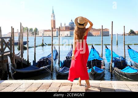 Vue arrière de la belle fille en robe rouge marchant dans Venise avec gondoles amarrées Banque D'Images