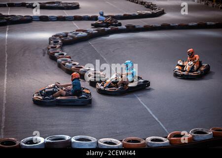 Trois gars se prennent les uns les autres sur une piste de karting intérieure Banque D'Images