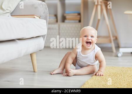 Photo horizontale d'un bébé joyeux et amusant assis sur le sol dans le salon, jouer et rire, copier l'espace Banque D'Images