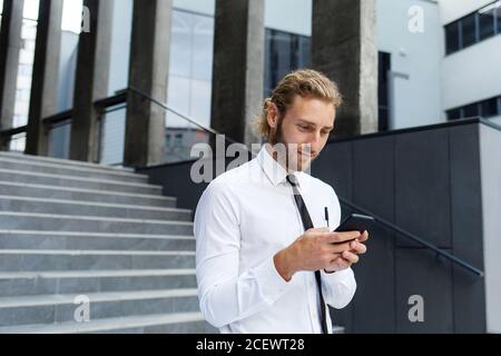 Portrait d'un jeune homme d'affaires prospère. Un homme aux cheveux bouclés dans une chemise blanche avec un téléphone sur le fond d'un centre d'affaires moderne Banque D'Images