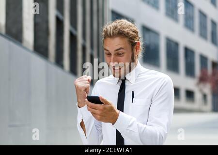 Portrait d'un jeune homme d'affaires prospère. Un homme aux cheveux bouclés dans une chemise blanche avec un téléphone sur le fond d'un centre d'affaires moderne Banque D'Images