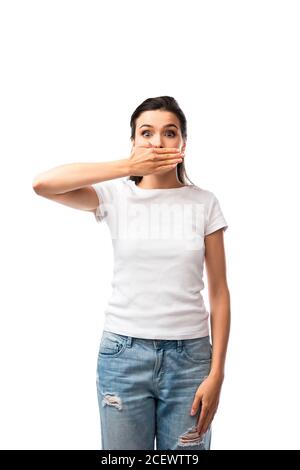 femme choquée en t-shirt blanc et jeans couvrant la bouche isolée sur blanc Banque D'Images