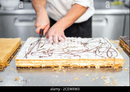 Gros plan d'un chef pâtissier coupant un grand gâteau en portions à la pâtisserie. Vidéos 4k de haute qualité Banque D'Images