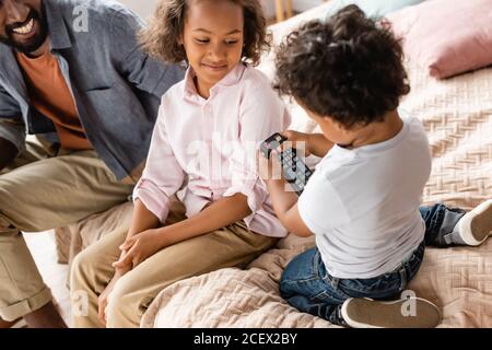 vue courte sur l'homme et la fille afro-américains assis lit près du garçon tenant la télécommande du téléviseur