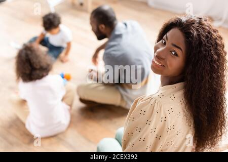 mise au point sélective d'une femme afro-américaine regardant la caméra à proximité famille jouant à l'étage Banque D'Images