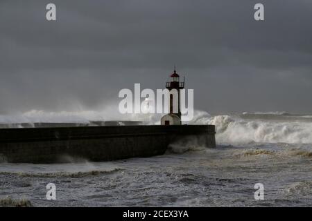 Grandes vagues blanches sur les jetées et le phare contre un ciel sombre et nuageux avant la pluie. Col du fleuve Douro, Porto, Portugal, pendant la tempête de la mer. Banque D'Images