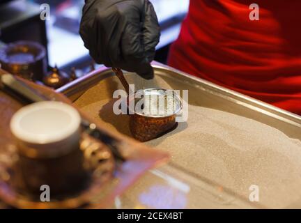 Faire du café sur le sable en gros plan, du café turc sur un marché, un homme en gants noirs agite du café dans la turka Banque D'Images