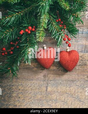Décoration de Noël sur fond de bois. Deux coeurs brillants rouges accrochés à une branche d'arbre de Noël. Saint-Valentin, l'amour en Noël, l'espace de copie Banque D'Images
