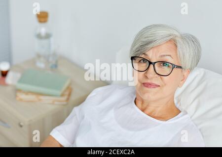 Portrait d'une femme mature de race blanche portant des lunettes de vue se rétablissant à l'hôpital quartier regardant la caméra Banque D'Images