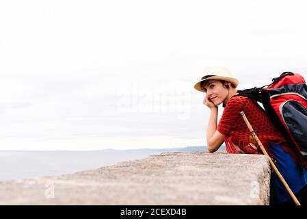 Vue latérale de jeunes femmes pèlerin avec sac à dos et bâton de trekking debout sur la côte de mer en regardant loin pendant Voyage le long de Camino de Santiago en Espagne Banque D'Images