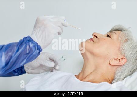 Travailleur médical méconnaissable portant un uniforme de protection prenant le nez d'une femme âgée écouvillon pour test du coronavirus Banque D'Images