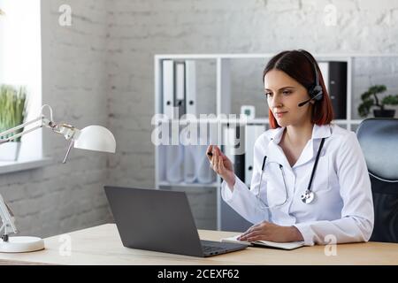 Femme médecin consulte par appel vidéo. Assistance médicale en ligne. Vidéoconférence de professionnels de la santé. Portrait d'un médecin sur le lieu de travail Banque D'Images