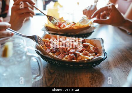 Vue latérale de crop anonyme personnes assis à une table en bois et manger des frites au bacon de délicieux en-cas tout en ayant la réunion à l'intérieur café Banque D'Images